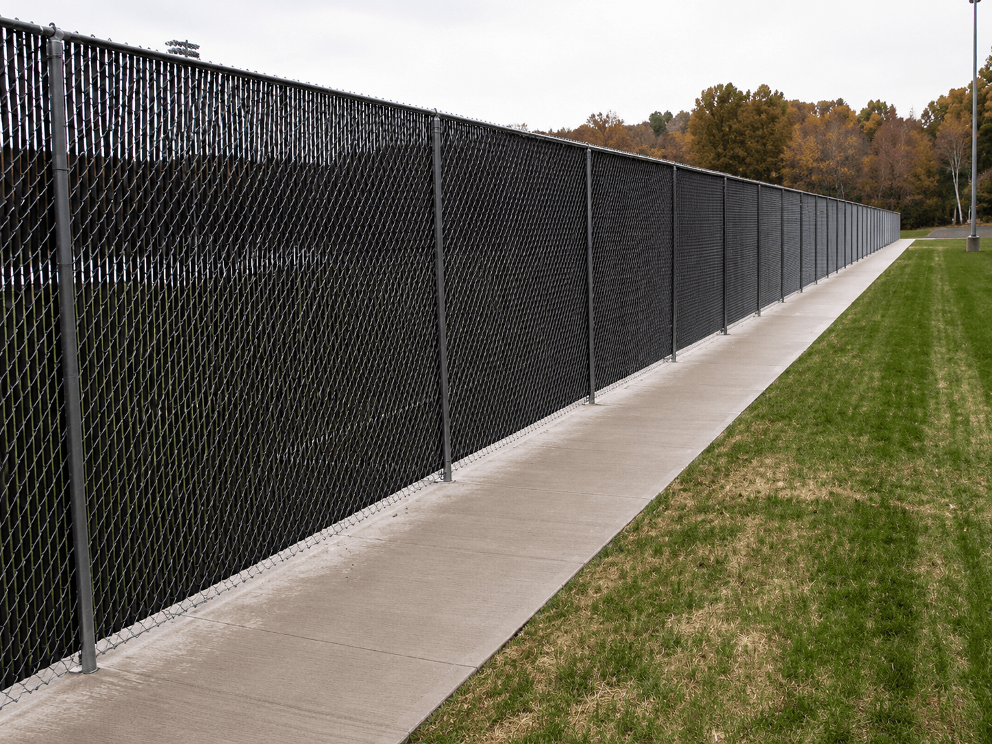 Chain-link fence with black privacy slats along an athletic field walkway