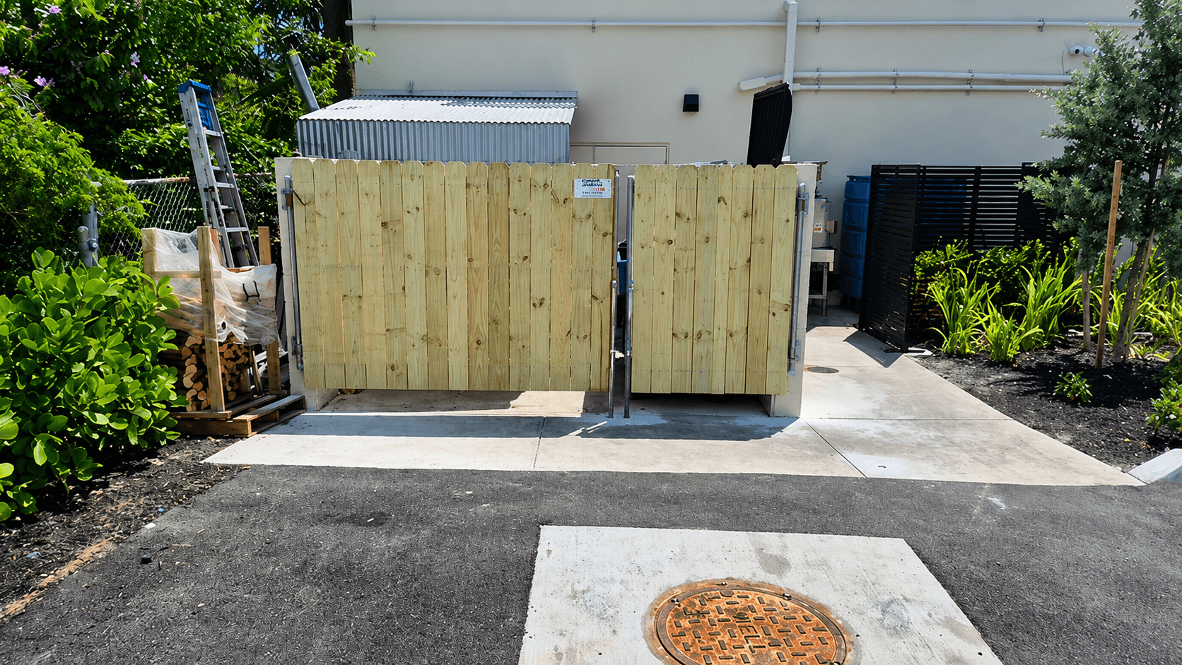 Double wood picket dumpster enclosure gates on a concrete pad at a commercial site