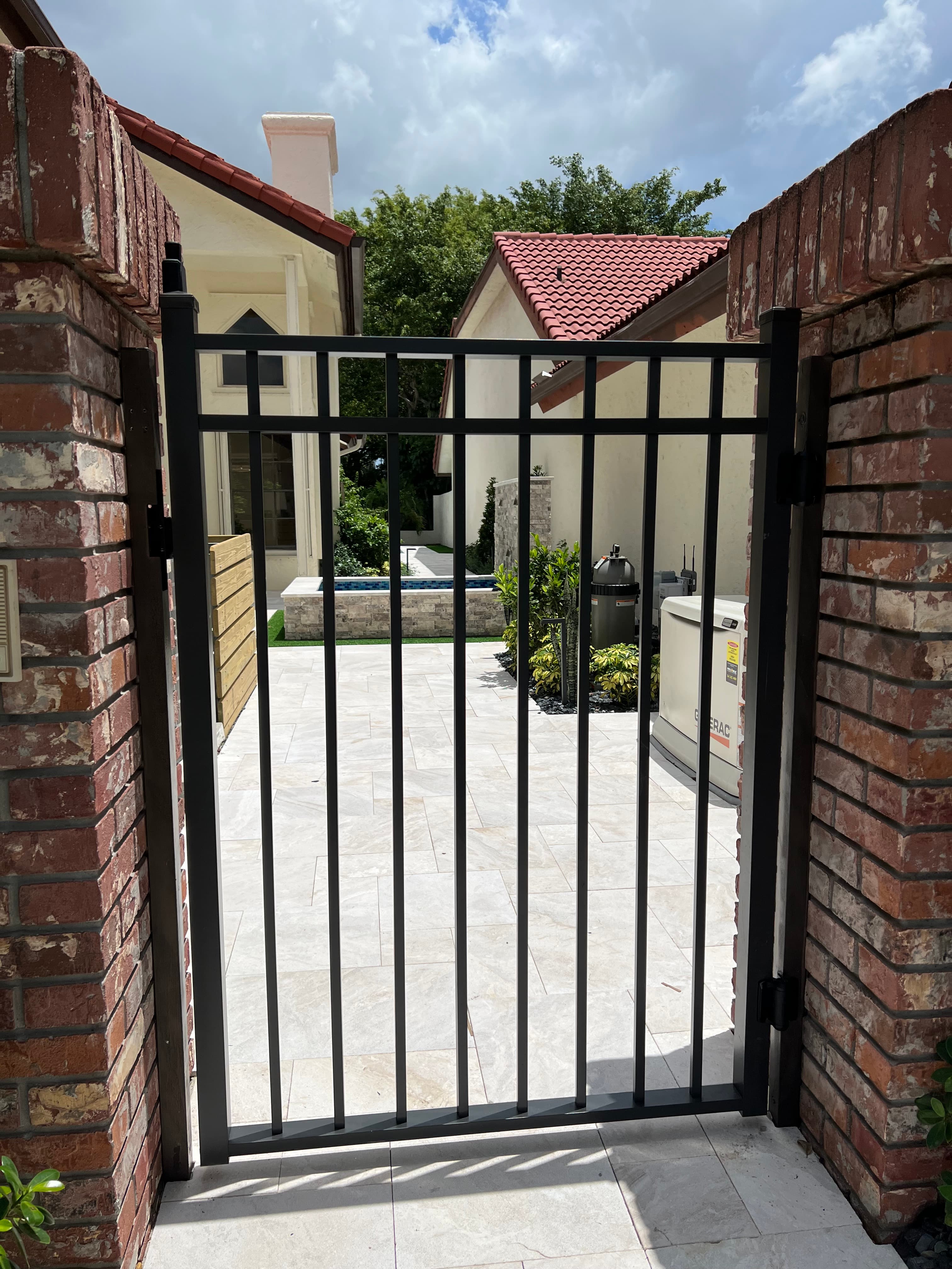 Matte black flat-top metal gate between brick pillars opening to a backyard patio