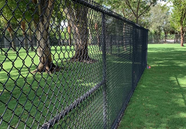 Black vinyl-coated chain link fence enclosing a shaded grass yard