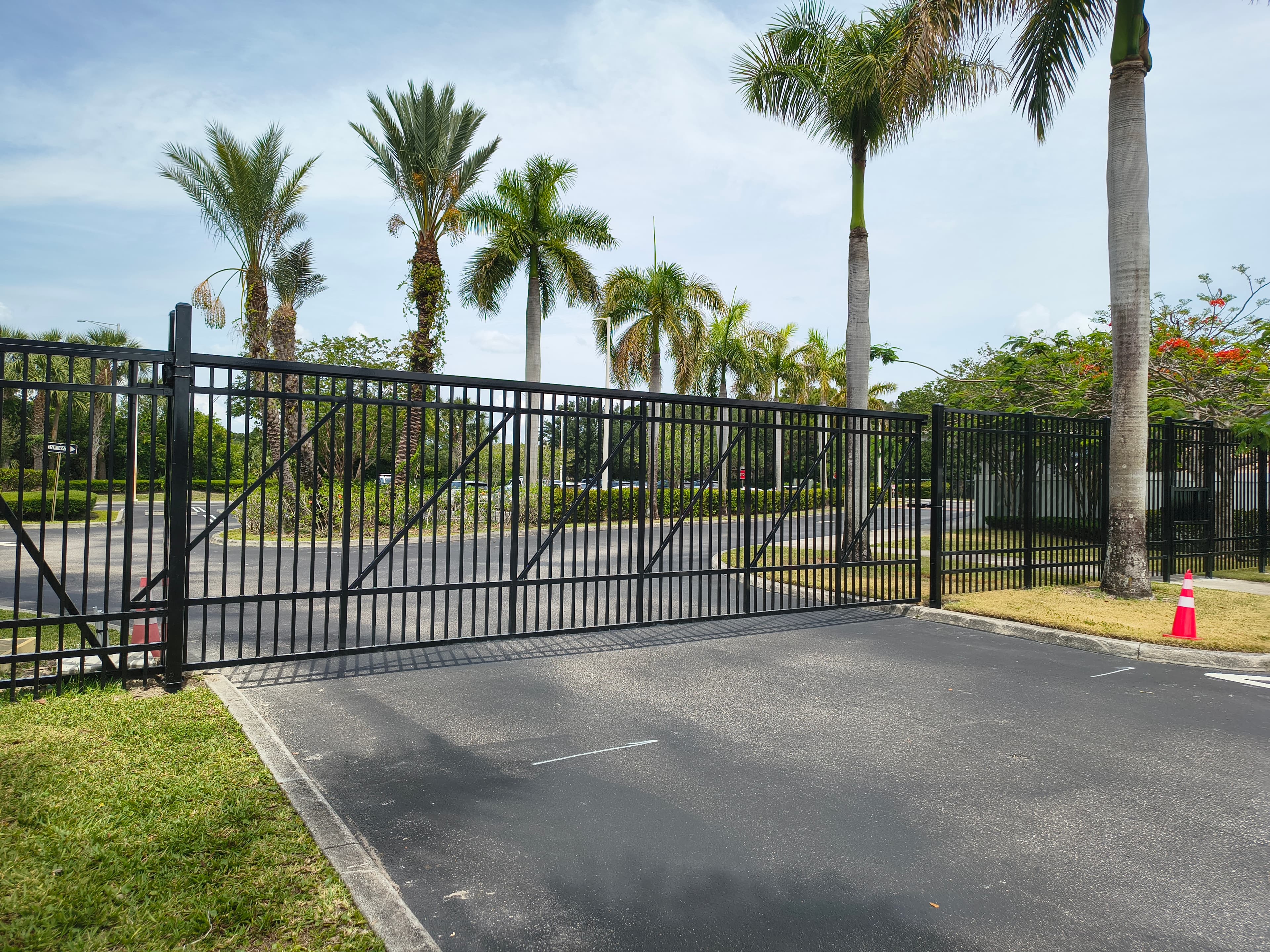 Wide black picket security gate with diagonal bracing across an asphalt drive
